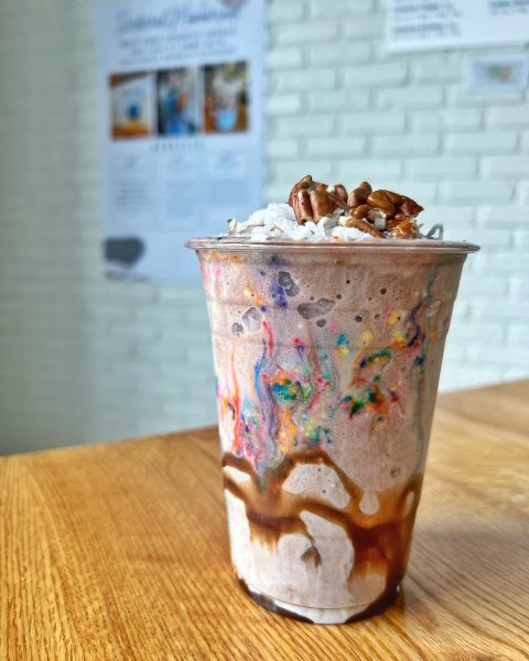 A cup of ice cream with whipped cream and pecans.