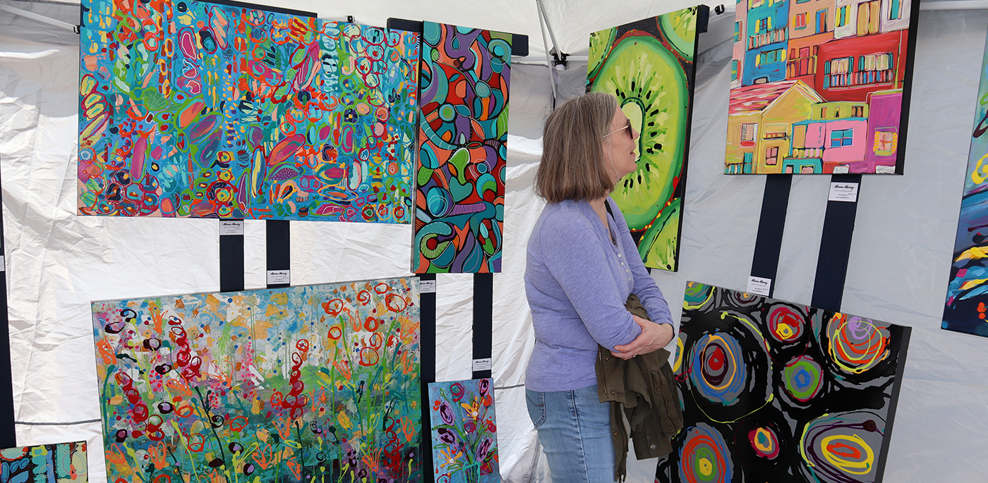 A woman looking at paintings in a tent.