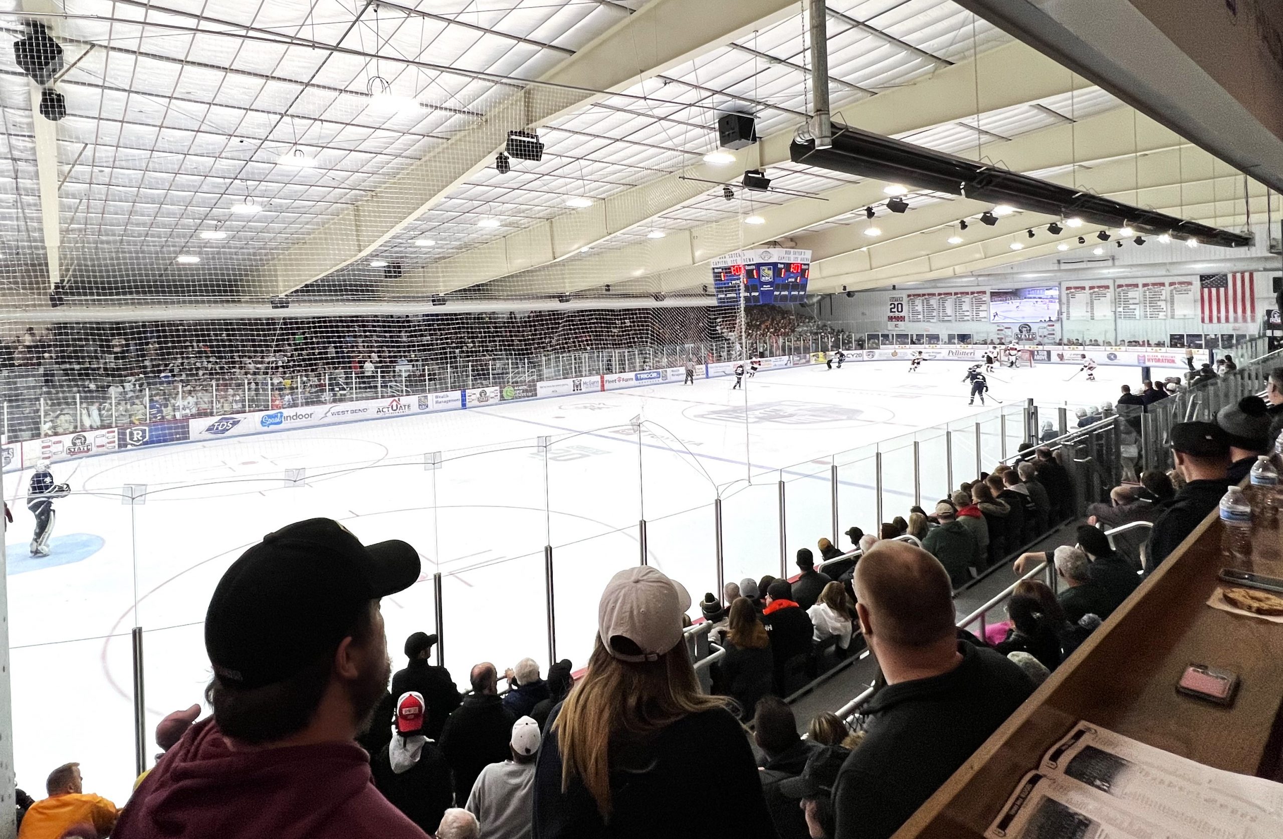 Spectators watch a hockey game in a large indoor arena. The ice rink is illuminated, and the crowd fills the stands.