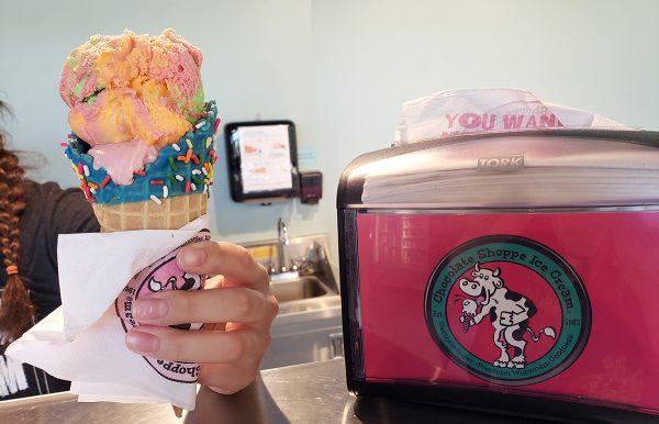 Chocolate Shoppe Ice Cream shop, person holding multi-colored ice cream cone next to pink napkin dispenser.