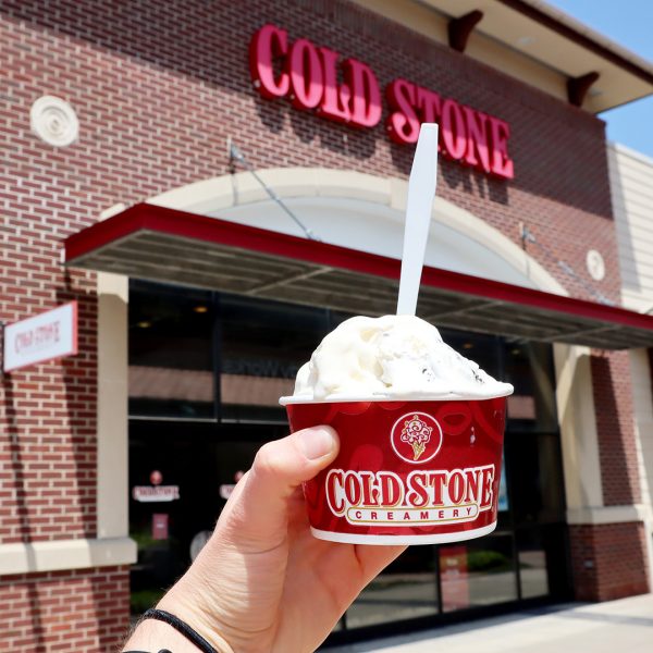 A person holding a cup of ice cream in front of a cold stone store.