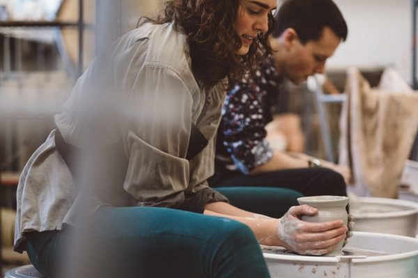 Two people are focused on shaping clay on pottery wheels in a workshop setting.