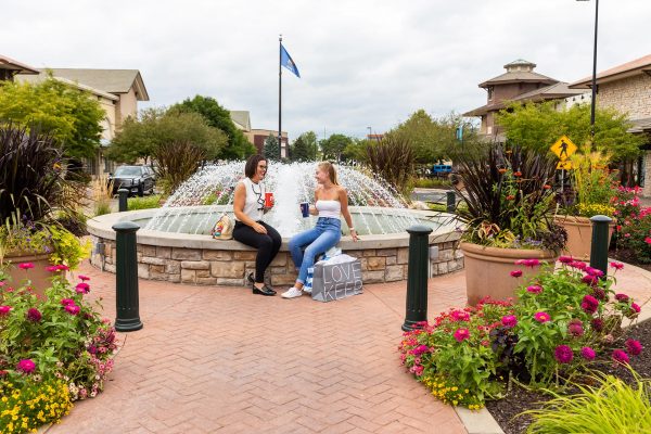 two women sitting on a fountain talking and drinking