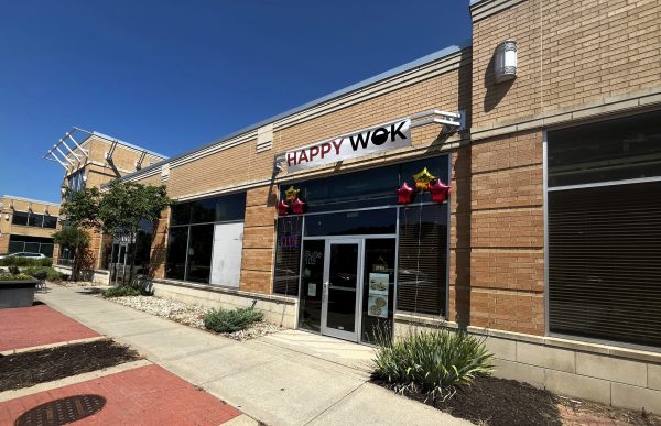 Exterior of a brick building with a sign reading "Happy Wok," glass door, five star-shaped balloons, and a small landscaped area by the entrance of this welcoming Chinese restaurant.