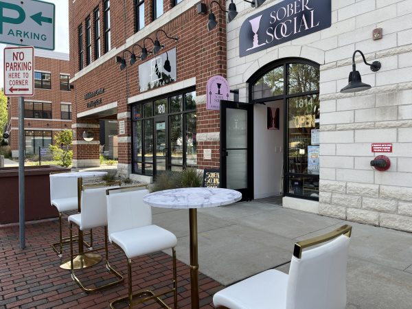 Outdoor seating and entrance of "Sober Social" café located on a brick-paved sidewalk adjacent to a commercial building. A "No Parking Here to Corner" sign is nearby.