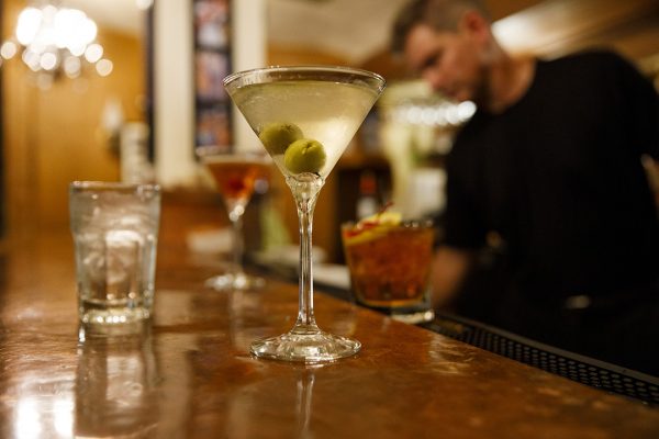 A bartender pours a martini into a glass.