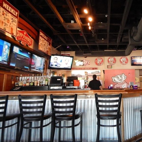 A bar interior with empty black chairs at the counter, multiple TVs on the wall, and drink bottles behind the bar—perfect for planning your Spring itinerary while a bartender stands in the background.
