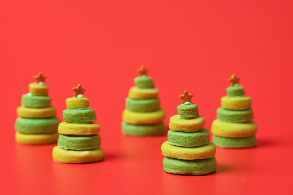 Stacked green and yellow cookies shaped like Christmas trees with small star toppings, set against a red background.
