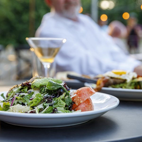 A man sits at a table with a plate of food and a glass of wine.