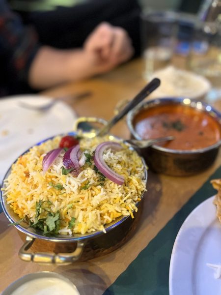 A plate of biryani garnished with onions and cilantro, accompanied by a bowl of curry.