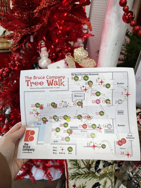 Hand holding a map titled "The Bruce Company Tree Walk" by Christmas decorations and tree.