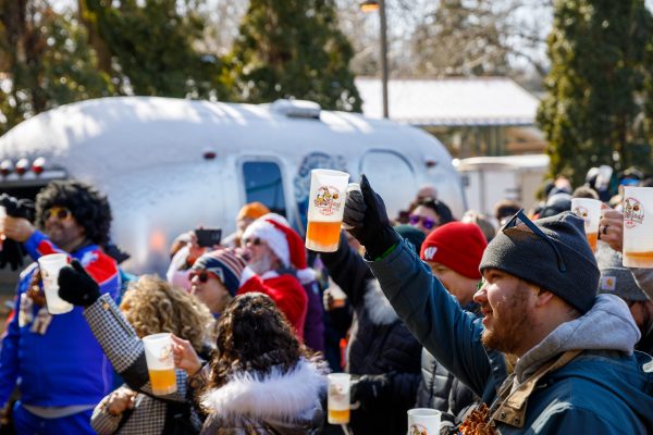 At Bockfest in Middleton, a lively group raises their cups of beer outdoors, surrounded by trees and the gleaming backdrop of an Airstream trailer.