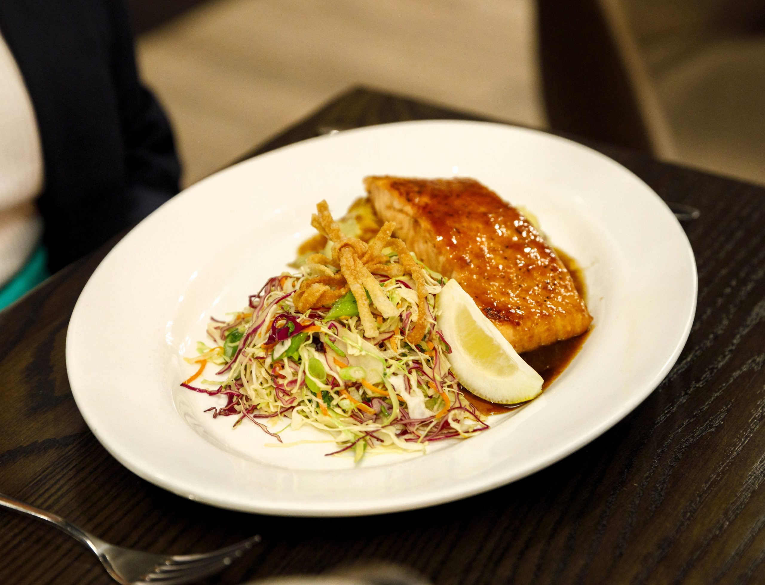 Plate with glazed salmon, a wedge of lemon, and a salad of shredded cabbage and fried onions, reminiscent of a Middleton fish fry favorite, served on a dark wooden table.