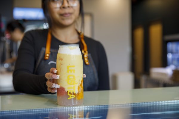 A person wearing glasses holds a cold beverage in a can labeled "Le Cistea." The drink contains fruit chunks and is placed on a glass surface.