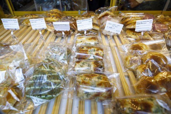 A bakery display showcasing various packaged pastries and bread rolls with labeled price tags, arranged on a wooden shelf.