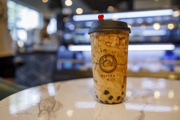 A plastic cup of bubble tea with a black lid and colorful straw sits on a white marble table in a well-lit café.